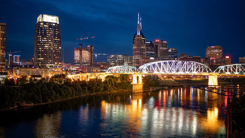 Illuminated buildings by river against sky at night