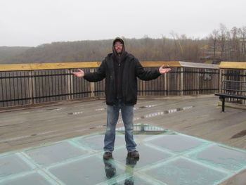 Portrait of young man standing on railing against sky