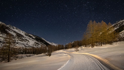 Road amidst snowcapped mountains against sky at night