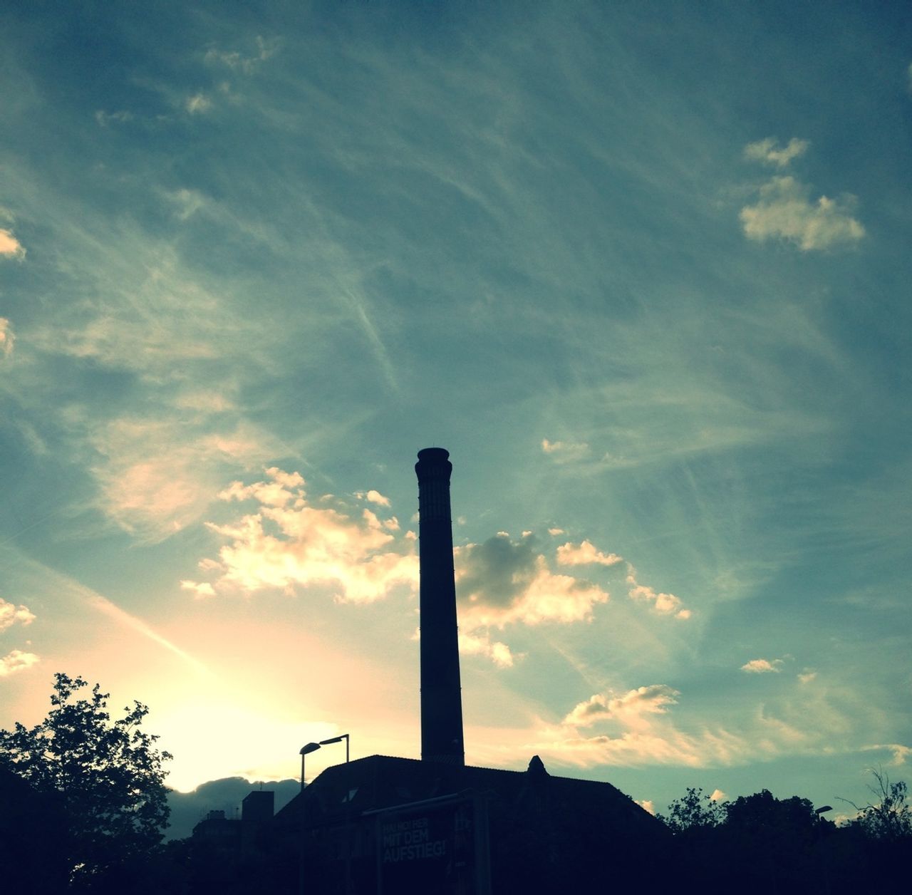 sunset, silhouette, low angle view, sky, built structure, cloud - sky, architecture, building exterior, tree, street light, cloud, sun, sunlight, orange color, nature, beauty in nature, cloudy, outdoors, no people, sunbeam