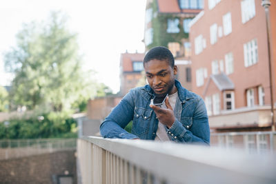 Young man talking on smart phone while standing by railing