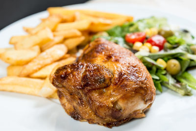 Close-up of roasted chicken with french fries and vegetables served in plate