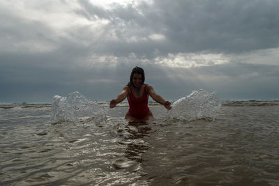 Portrait of young woman standing in sea against sky