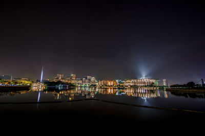 Illuminated city by river against sky at night