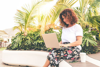 Smiling woman using laptop while sitting by tree