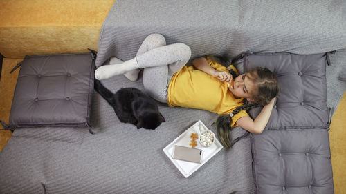 Directly above shot of girl relaxing on sofa with cat and food