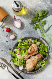 Baked chicken drumsticks and a green vegan salad made from a of green leaves and spring vegetables.