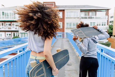 Back view of unrecognizable curly haired african american female friends walking with skateboards in city and enjoying weekend