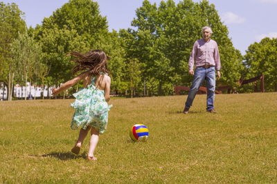 Rear view of granddaughter playing with grandfather at park