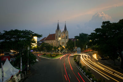 Light trails on road amidst buildings against sky at night