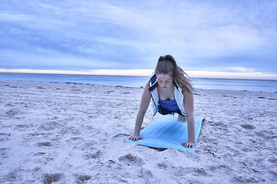 Woman exercising at beach against cloudy sky