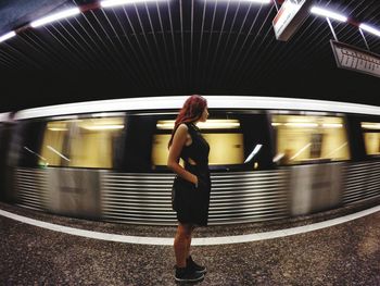 Side view of young woman standing with hand in pocket at subway station