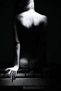 Rear view of naked woman sitting on bench in darkroom