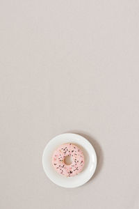Minimalistic sweetness banner. pink donut on a white plate on a beige background with copy space