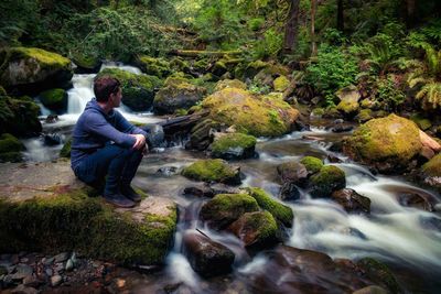 Woman sitting on rock by river in forest