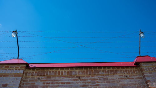 Low angle view of telephone pole against building against clear blue sky