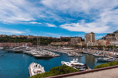 Sailboats moored in harbor by city against sky