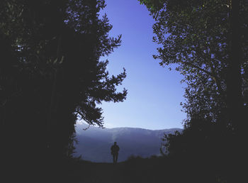 Rear view of silhouette man standing on mountain against clear blue sky