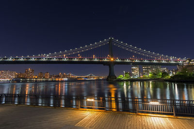 Illuminated manhattan bridge over east river against sky seen from pier