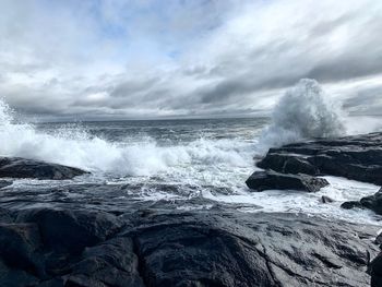 Waves splashing on rocks against sky