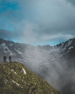People standing on cliff against mountain and sky