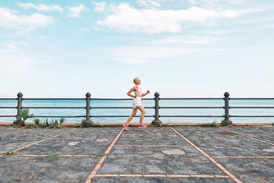 Young attractive sportive woman running on seaside promenade. workout outdoors by the sea. 