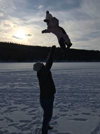 Father playing with daughter on snow covered field against sky