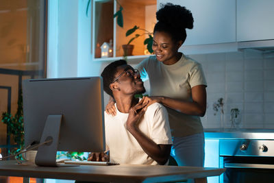 Woman hugging husband from behind while he working on computer remotely from home late at night