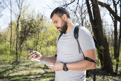 Young man using mobile phone while standing on tree