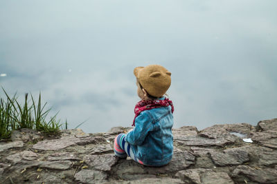 Toy sitting on rock by sea against sky