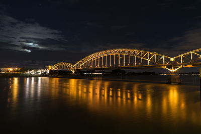 Illuminated bridge over river against sky at night