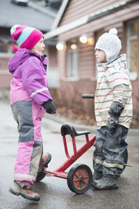Side view of elementary girls with tricycle standing at yard