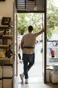 Rear view of male store owner leaning on doorway