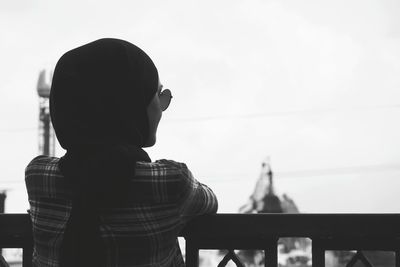 Rear view of man standing by railing against sky