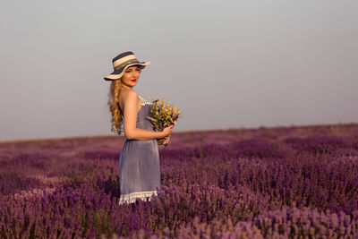 Young woman holding bouquet of wild flowers in lavender field at sunset