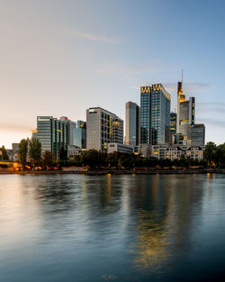 Illuminated buildings by river against sky in city