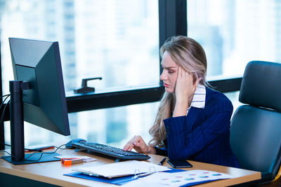 Businesswoman with headache using computer on desk in office