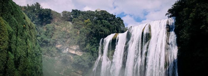 Panoramic view of waterfall in forest against sky