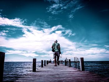 Man standing on wooden pier over sea against sky