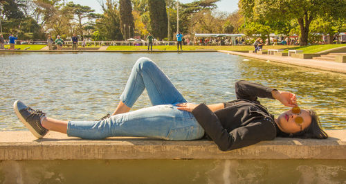 Woman relaxing on retaining wall by lake