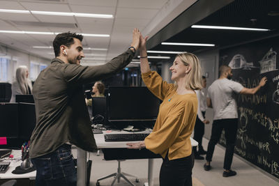 Male and female professional celebrating success while gesturing high-five at office desk