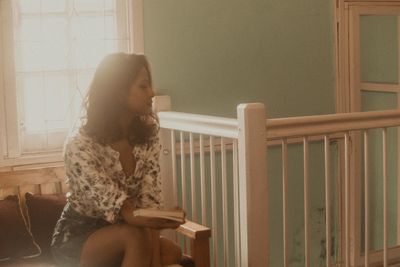 Young woman holding book while sitting by railing