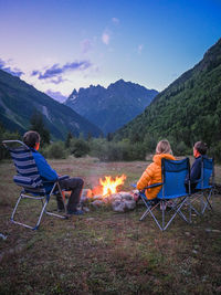 Three people sitting by the campfire watching the mountains.