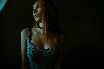 Woman looking away while standing against black background