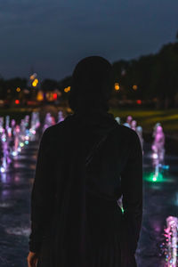 Rear view of man standing against illuminated city at night