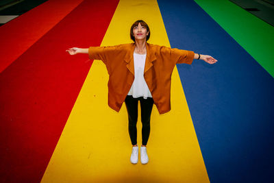 Full length portrait of woman standing against yellow wall