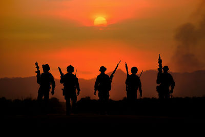 Silhouette people against orange sky during sunset