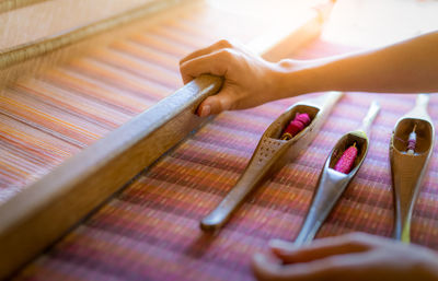 Cropped hand of woman holding wooden equipment with spool on table