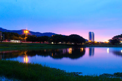 Scenic view of lake by illuminated buildings against blue sky
