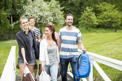 Group of happy friends with luggage walking by railing at park